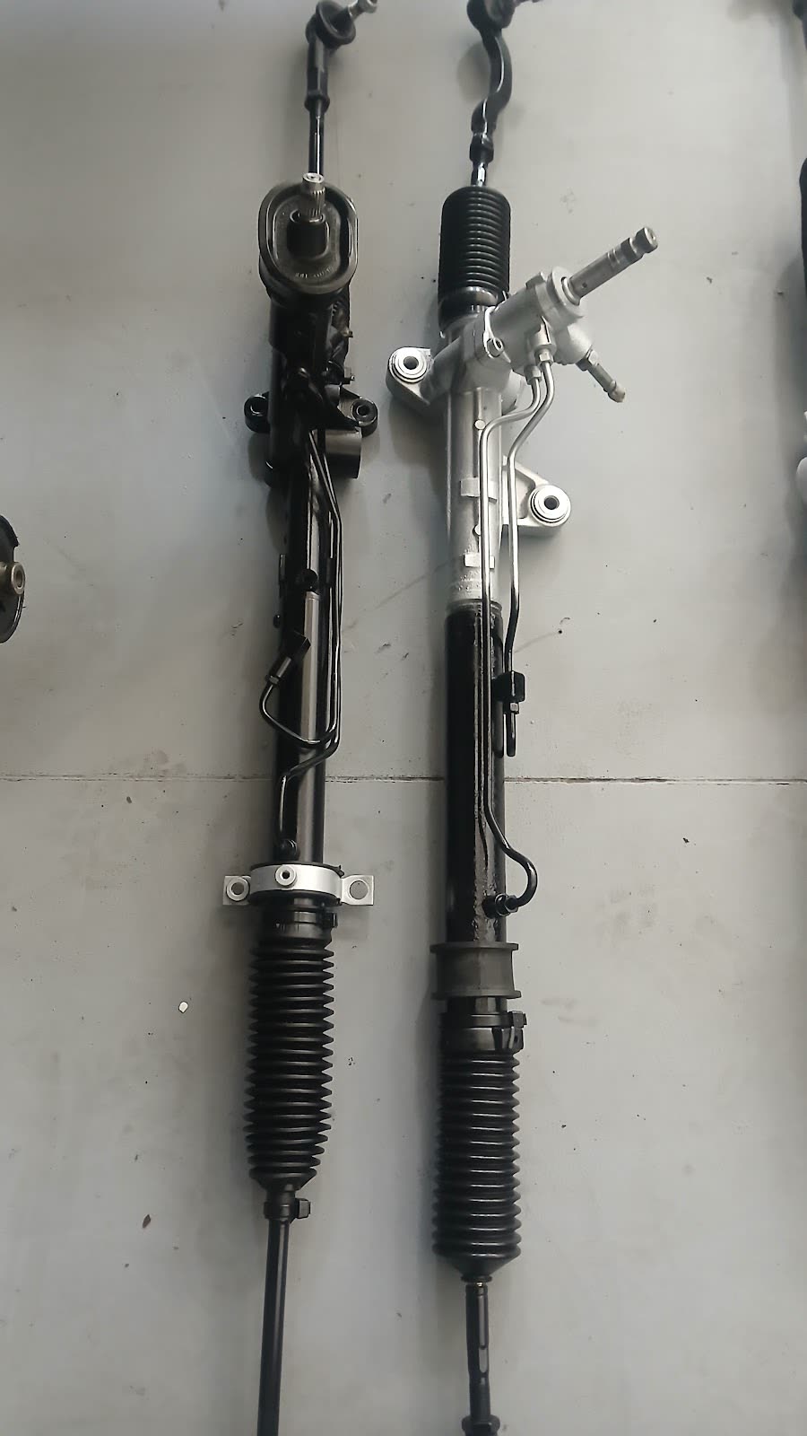 A worn steering rack beside a fully reconditioned steering rack